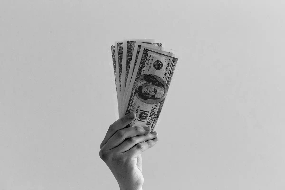 hellgrauer Hintergrund, eine Hand hält in der Mitte ein Bündel Geldscheine aufgefächert